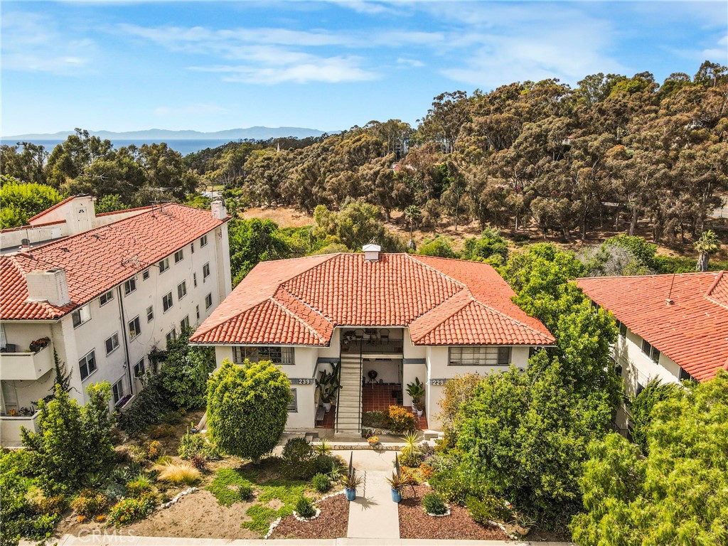 Aerial view of red-tile-roof residences, landscaped grounds, wooded hillside, and distant water.