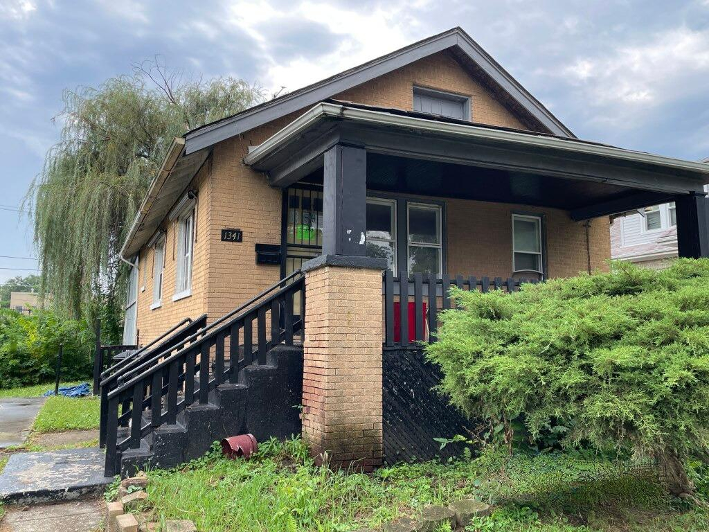 Tan brick home with a deep covered porch, black railings, and front steps.