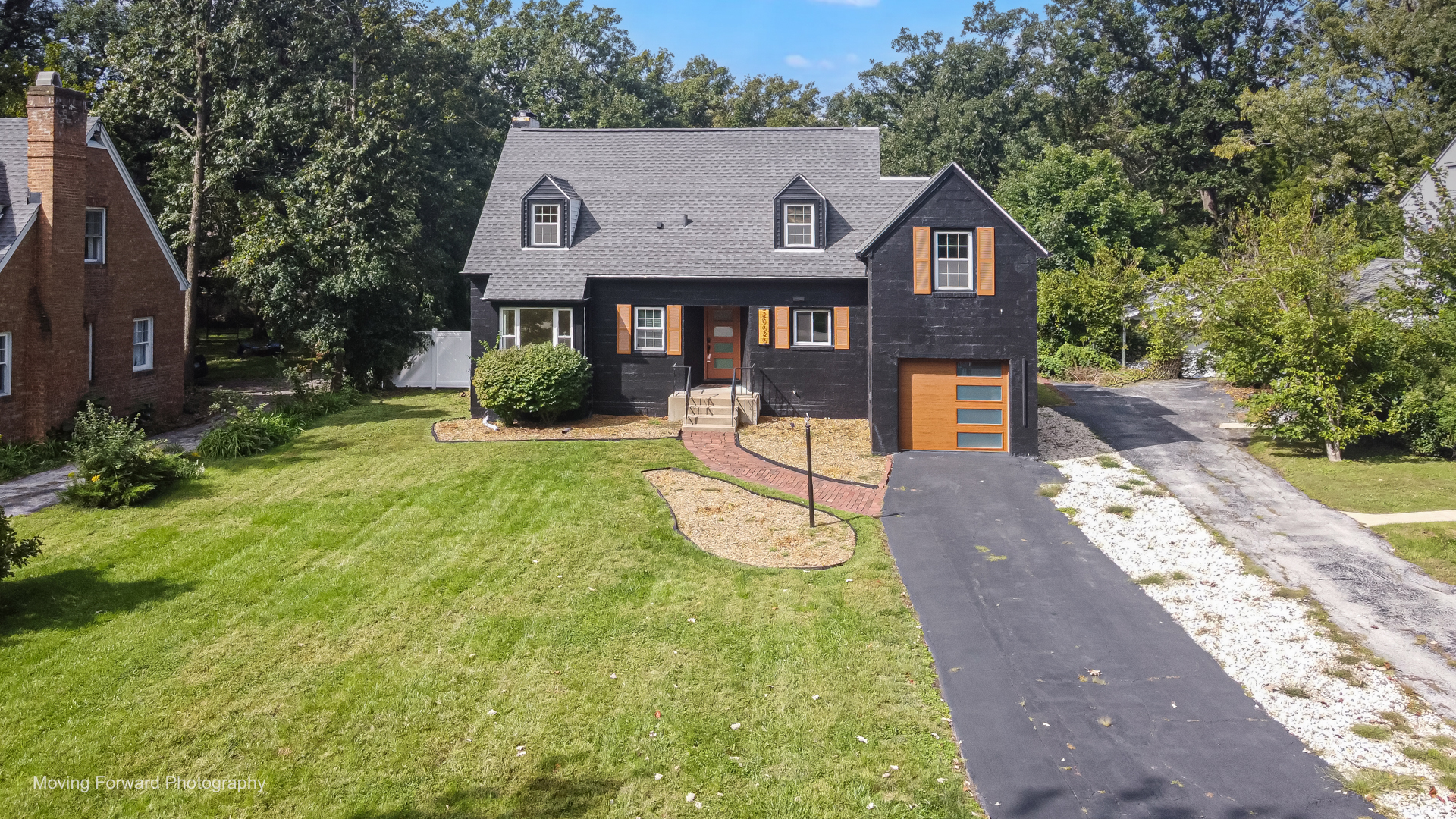 Dark two-story house with orange shutters, a matching garage door, and a curved brick walkway.