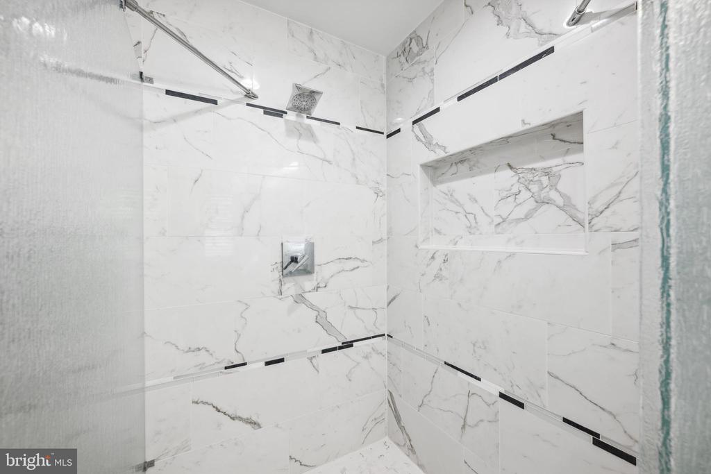 Marble-tiled walk-in shower with glass enclosure, recessed niche, and square overhead showerhead.