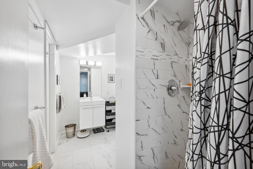 Bathroom with marble-look shower tile, mosaic accent strip, and geometric-patterned curtain.
