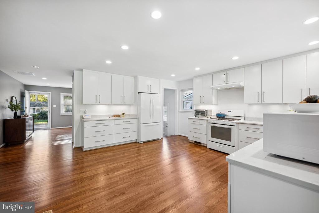 Bright white kitchen with stainless steel appliances, a large peninsula, and hardwood floors.