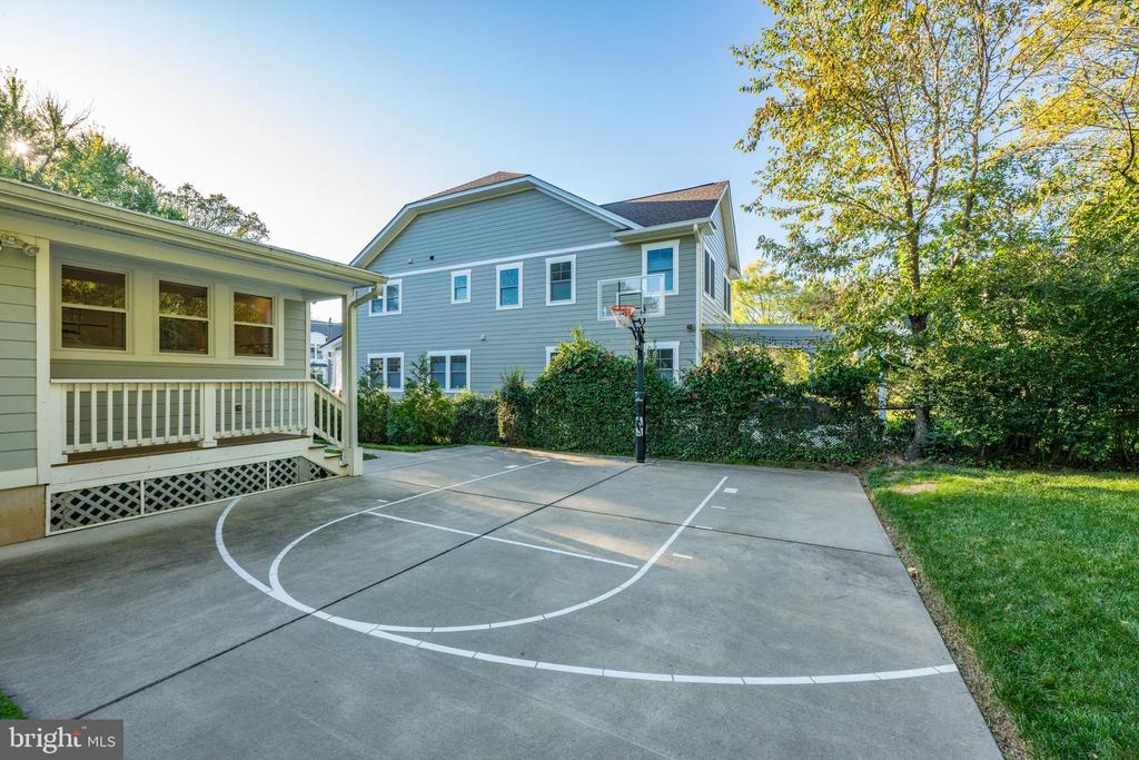 Backyard basketball court beside a covered porch, with a hoop and two-story blue house.