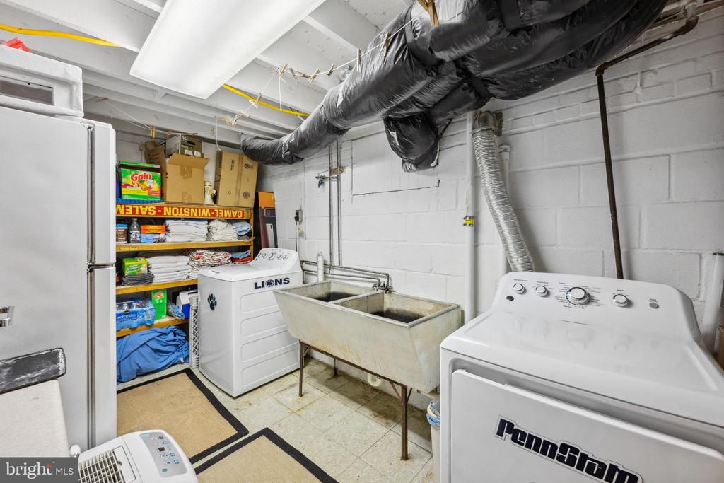 Basement laundry room with a deep utility sink, washer, dryer, and storage shelves.
