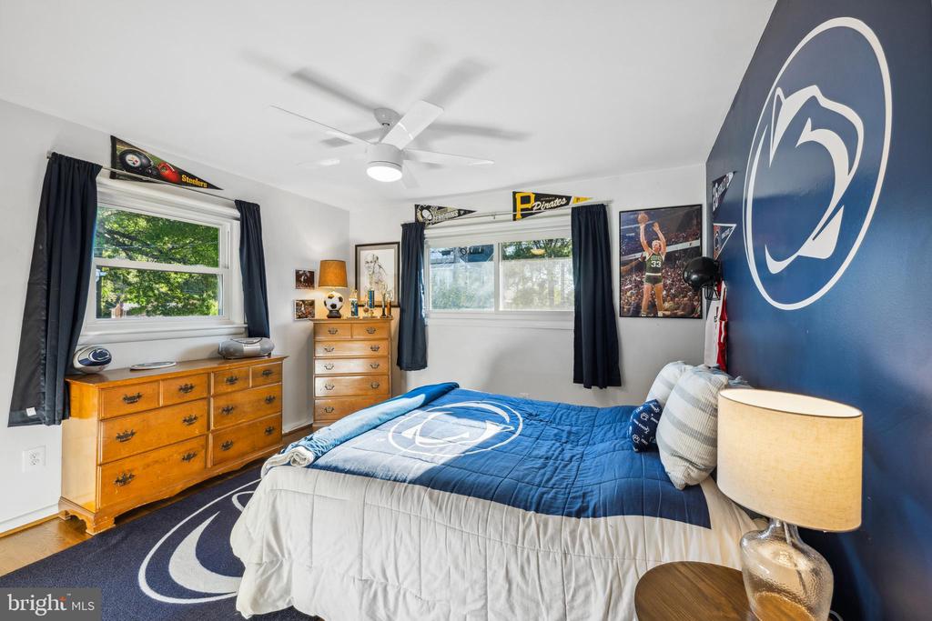 Bedroom with Penn State-themed bedding, a large wall logo, two windows, and wooden dressers.