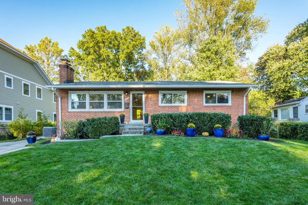 Single-story brick home with white-trimmed windows, clipped shrubs, and a broad green front lawn.