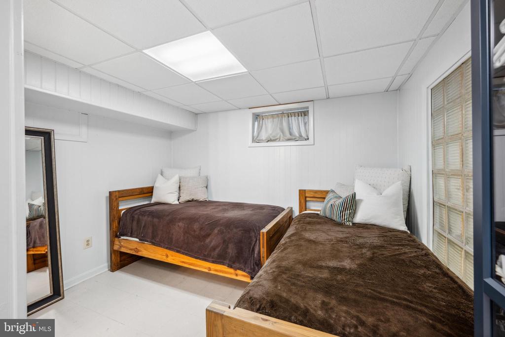 Bedroom with two wooden twin beds, brown blankets, and a small curtained window.