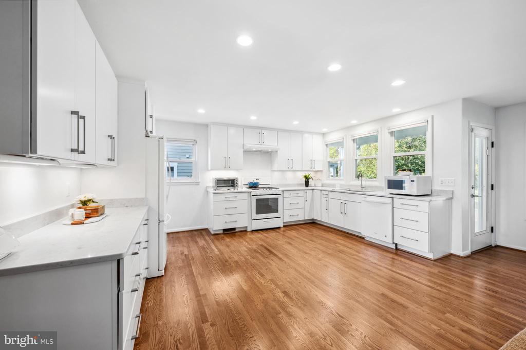 Bright white kitchen with stone countertops, stainless steel appliances, and warm hardwood floors.