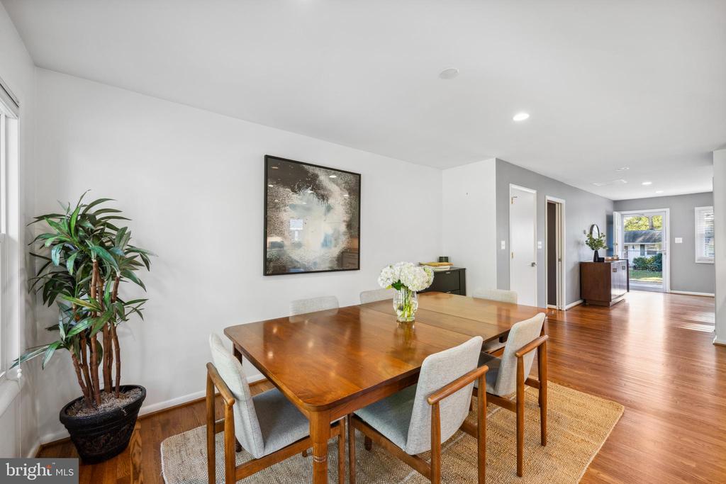 Dining room with a wooden table, upholstered chairs, white flowers, and hardwood floors.