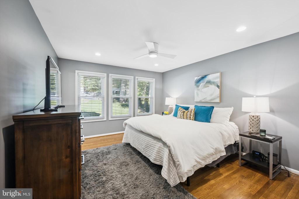 Bedroom with a white bed, teal pillows, three windows, and hardwood floors.