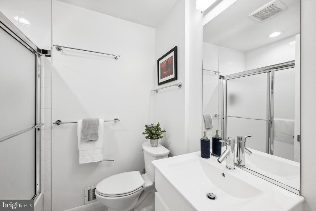 Bathroom with a glass shower, white vanity, and toilet topped with a small plant.