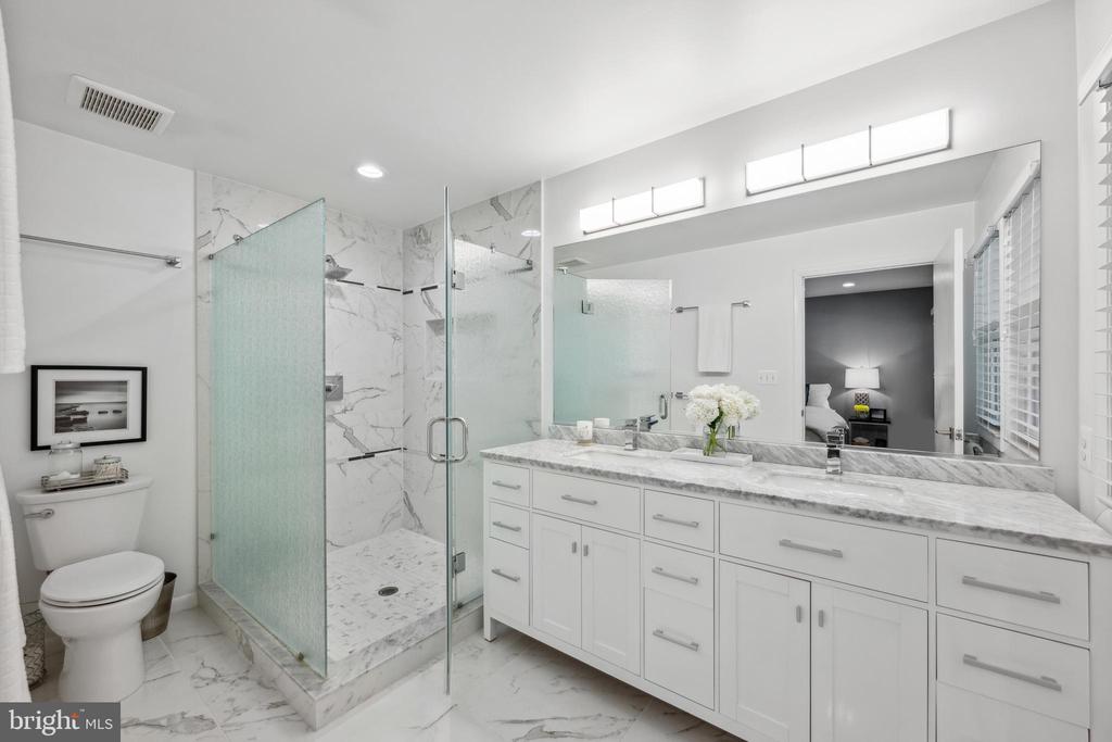 Bathroom with a marble-tiled walk-in shower and long white vanity with marble counters.
