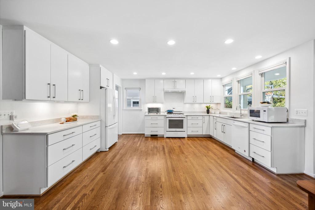 Bright white kitchen with extensive cabinetry, hardwood floors, and large windows above the sink.