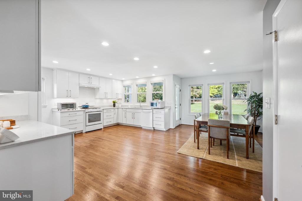 Open kitchen and dining area with white cabinets, hardwood floors, and windows overlooking the yard.