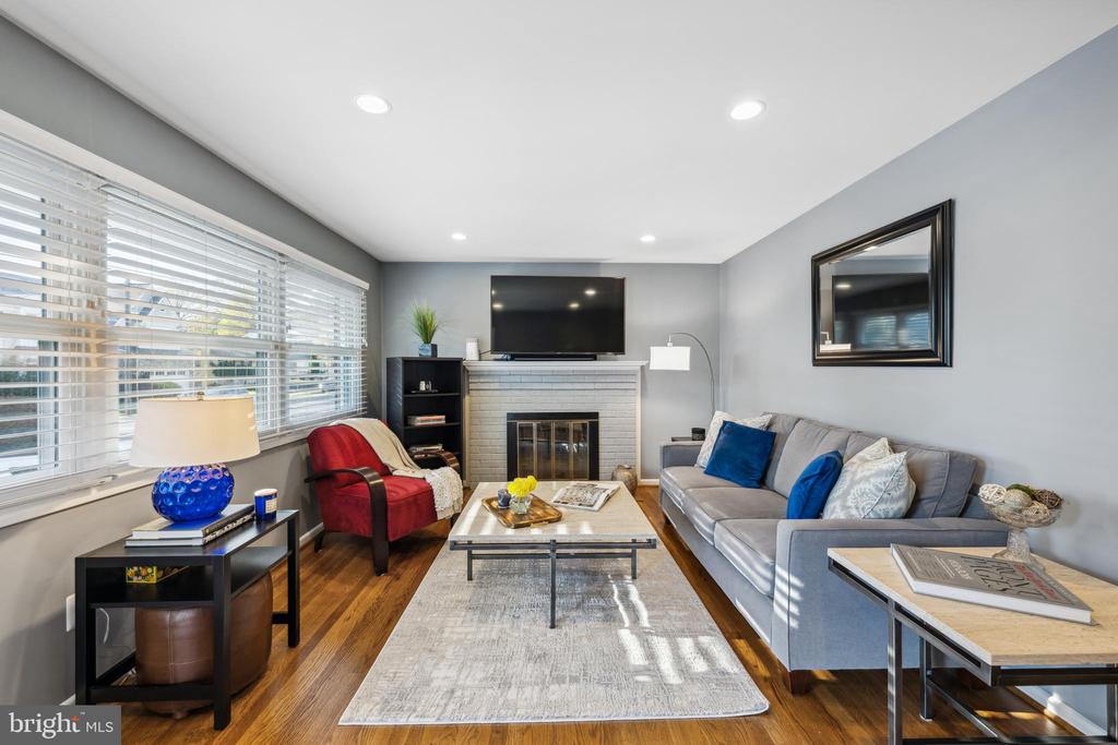 Furnished living room with a white fireplace, hardwood floors, large windows, gray sofa, and red armchair.