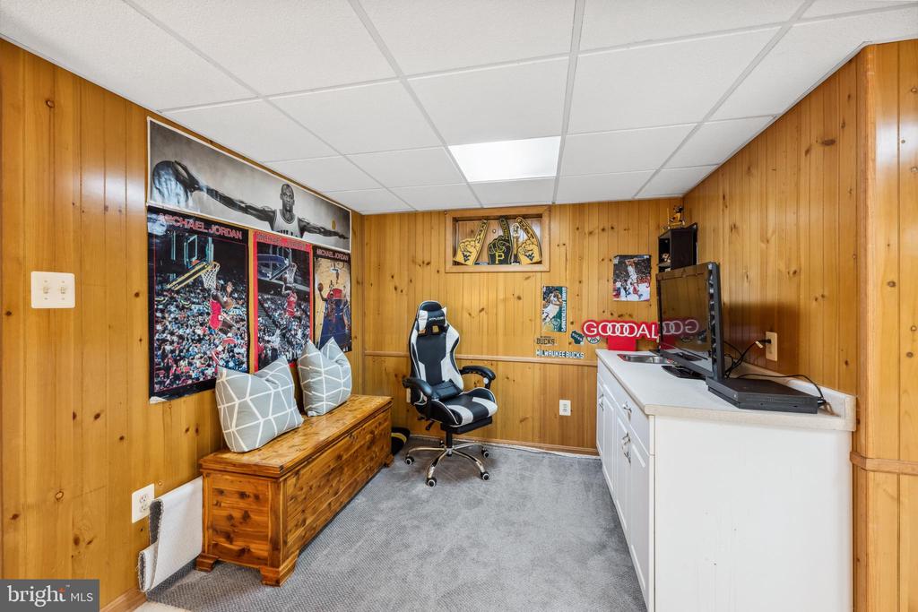 Wood-paneled finished room with a gaming chair, television setup, and basketball memorabilia.