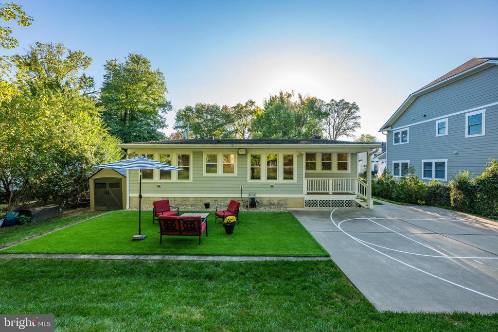 Rear of a single-story home with a broad lawn, outdoor seating, and a paved driveway.