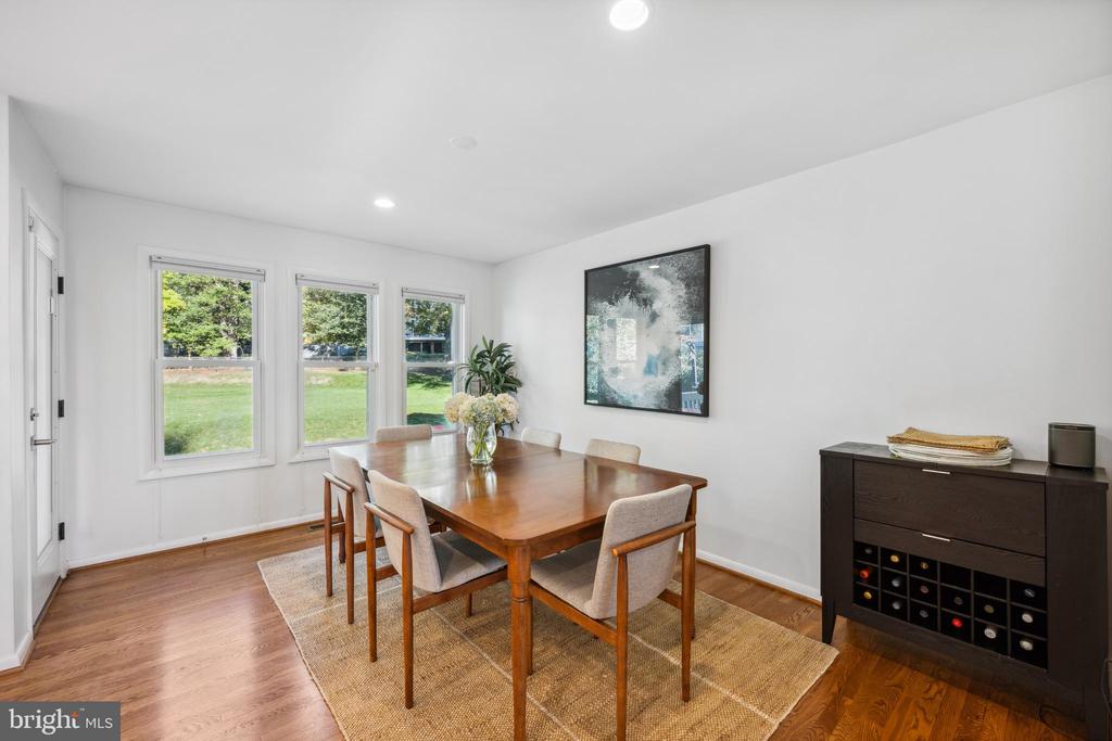 Dining room with a wooden table, three lawn-facing windows, hardwood floors, and a dark wine cabinet.