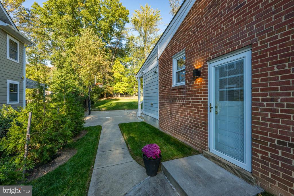 Home entrance with brick wall, concrete walkway, potted flowers, and a basketball hoop in the yard.
