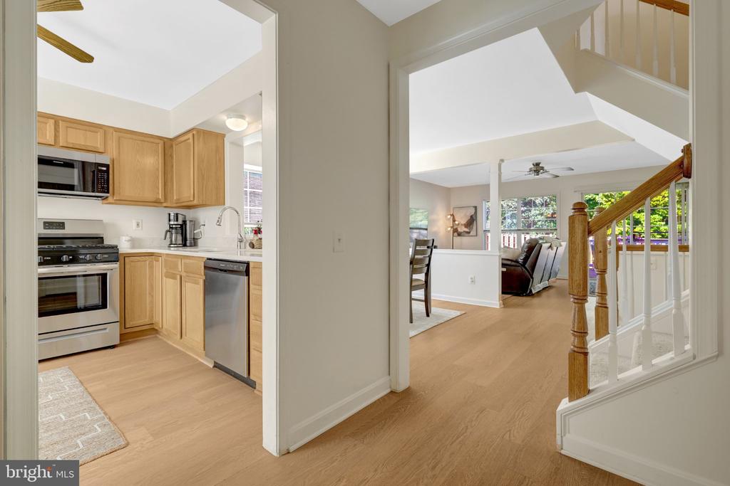 Kitchen and adjoining living area with light wood cabinets, stainless appliances, and a wood-and-white staircase.