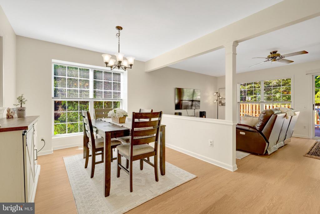 Dining area with dark wood furniture and large windows, opening to a living room with leather seating.