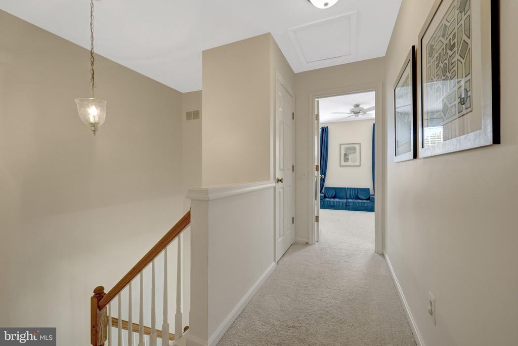 Upstairs hallway with carpeted floors, a wooden stair railing, and a blue sofa visible through the doorway.