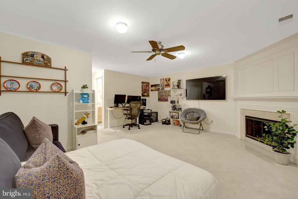 Bedroom with a bed, desk workspace, wall-mounted television, and fireplace.