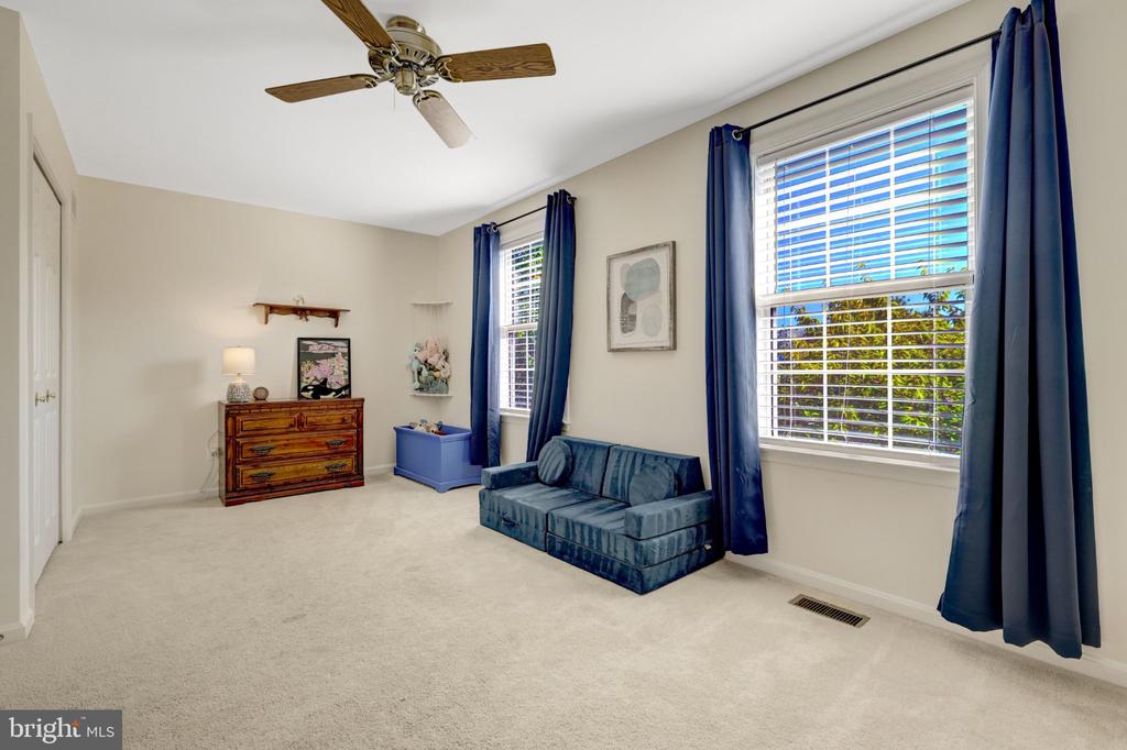 Furnished bedroom with a blue sofa, wooden dresser, and two windows framed by navy curtains.