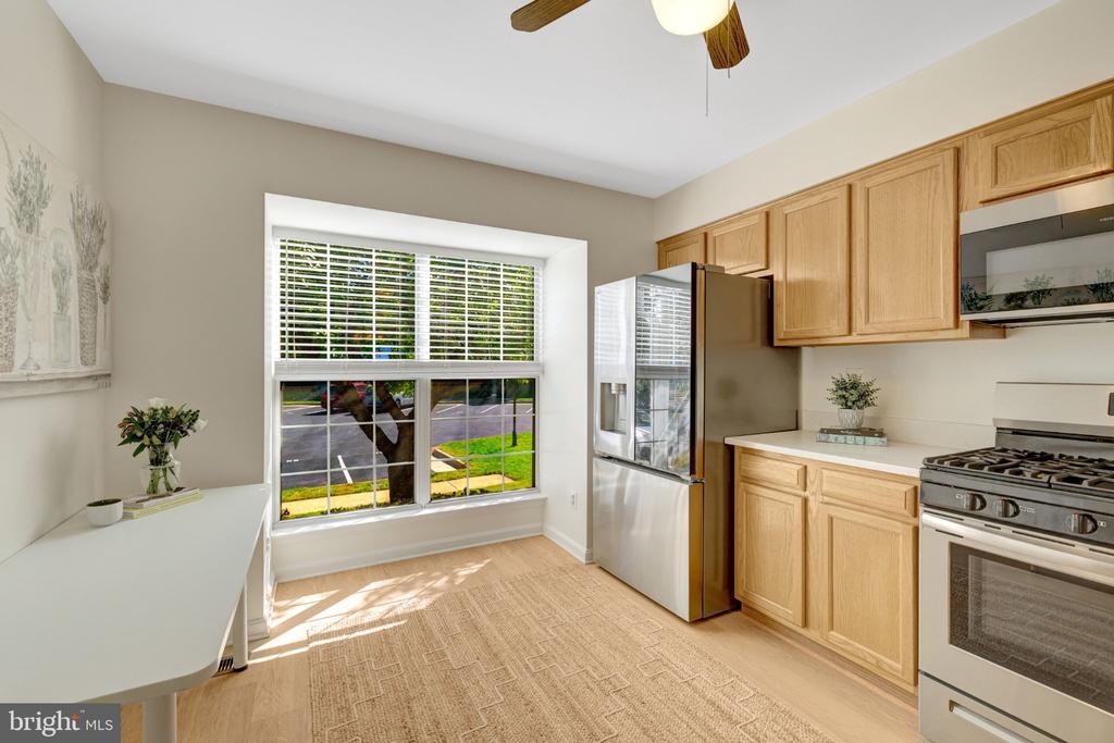 Kitchen with light wood cabinets, stainless steel appliances, and a large window overlooking a lawn.