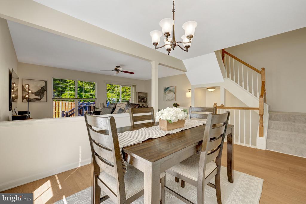 Dining room with a dark wood table, chandelier, floral centerpiece, and staircase beside the open living area.