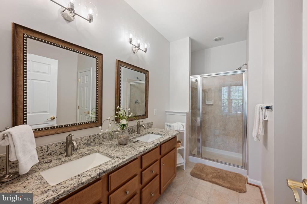 Bathroom with a double-sink granite vanity and a tiled glass-enclosed shower.
