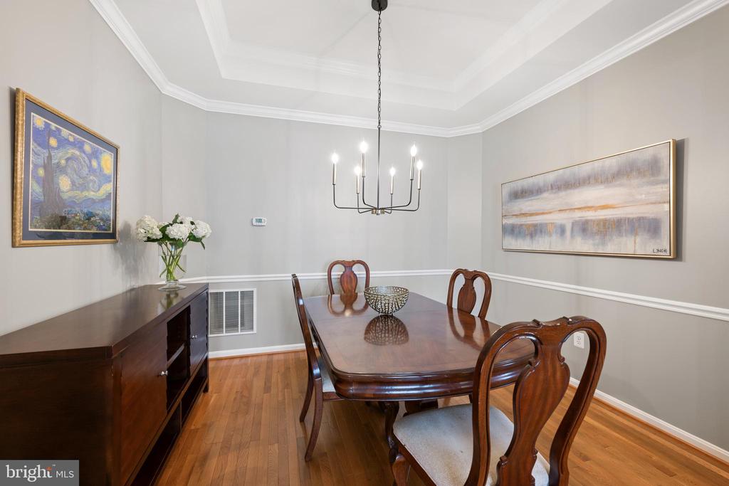 Dining room with a dark wood table, chandelier, hardwood floors, and tray ceiling.