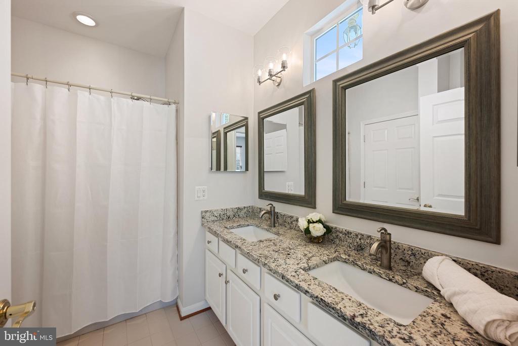 Bathroom with a double-sink granite vanity, dark-framed mirrors, and a white shower curtain.