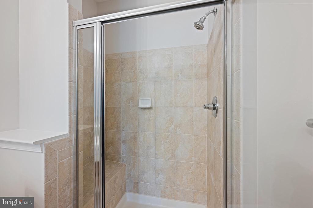 Tiled bathroom shower with a glass enclosure, built-in seat, and wall-mounted showerhead.