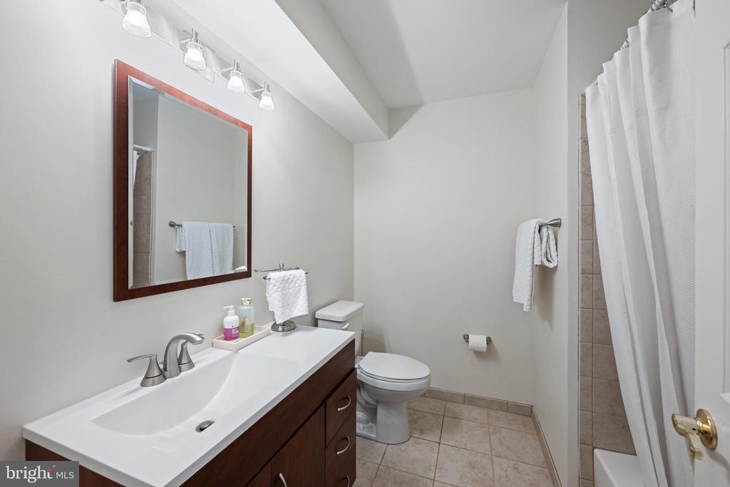Bathroom with a dark wood vanity, framed mirror, toilet, and white-curtained tub-shower.