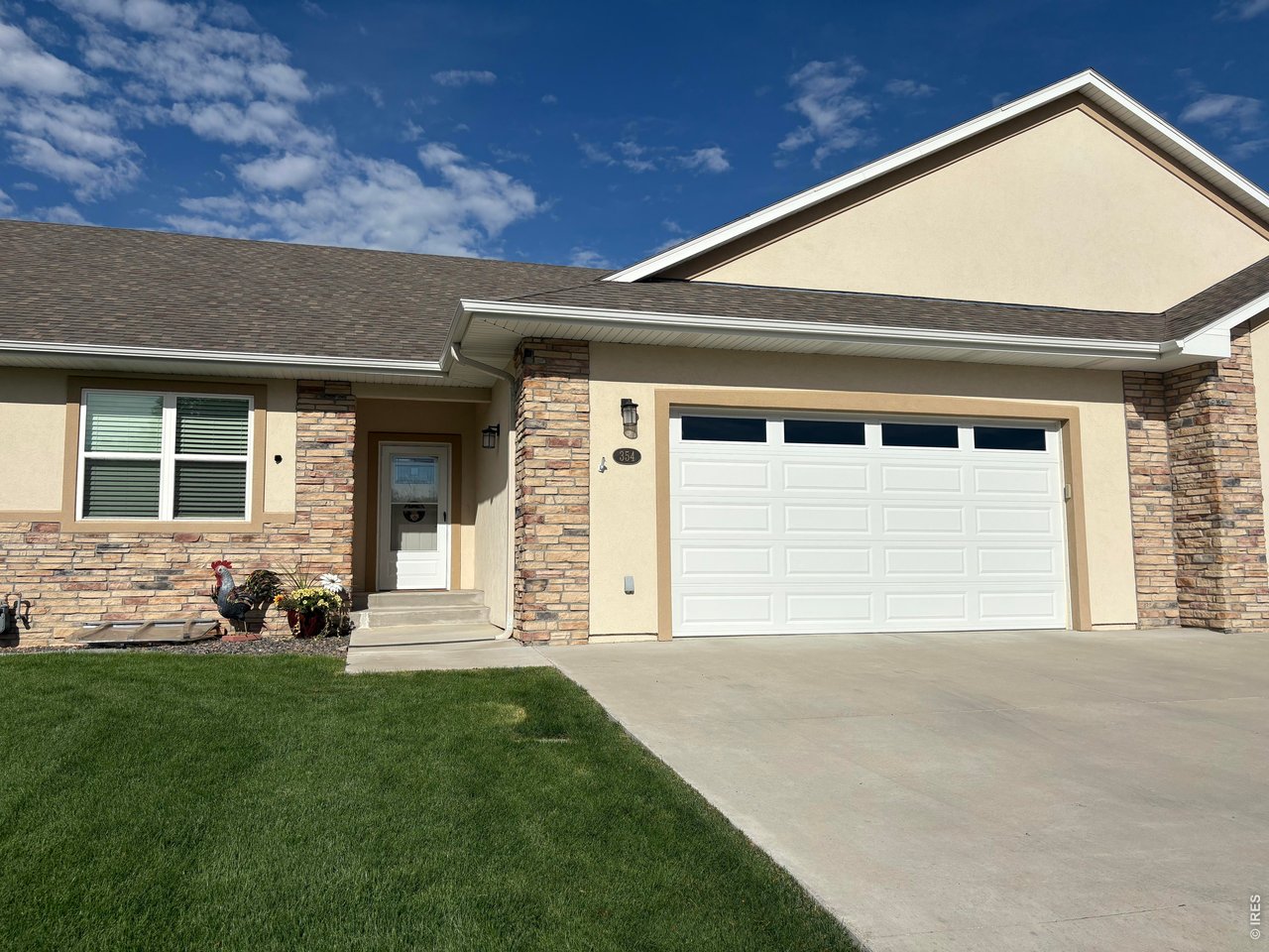 House exterior with stone accents, a white double garage door, green lawn, and wide driveway.
