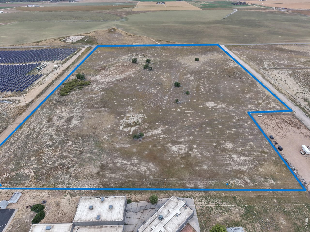 Aerial view of vacant land outlined in blue beside solar panels and farm fields.