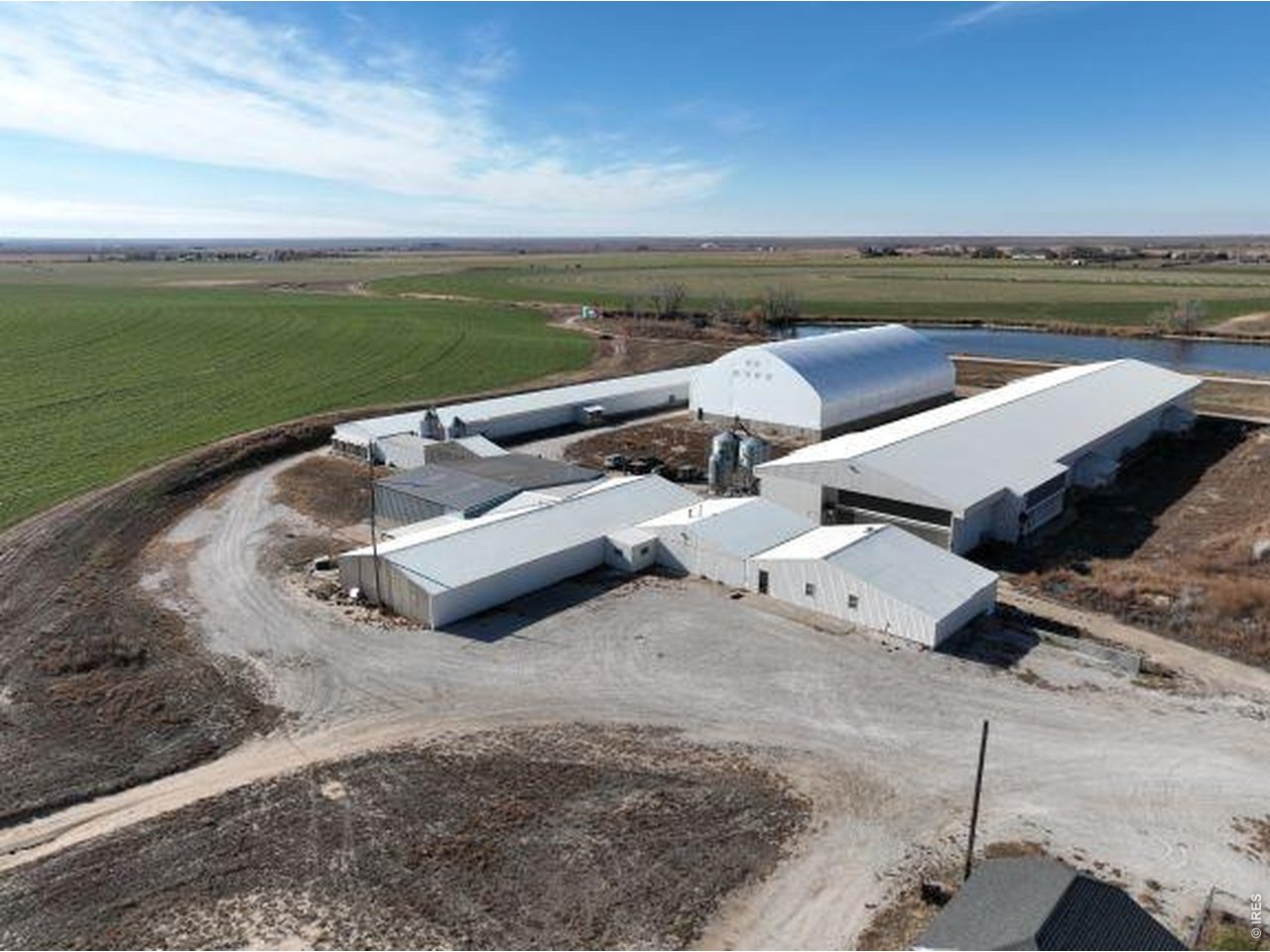 Aerial view of white agricultural buildings surrounded by fields and gravel drives.