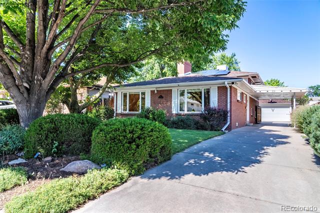 Red-brick house with a wide driveway, attached garage, and mature trees in the front yard.