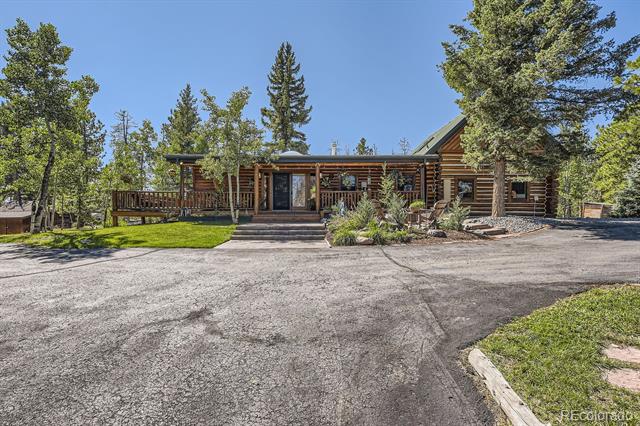 Log home with a covered porch and landscaped entrance beside a broad paved driveway.
