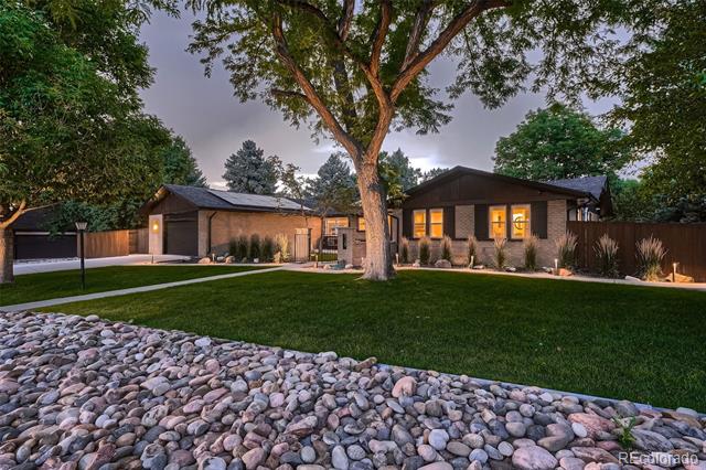 Single-story home at dusk with glowing windows, a large front-yard tree, and landscaped lawn.