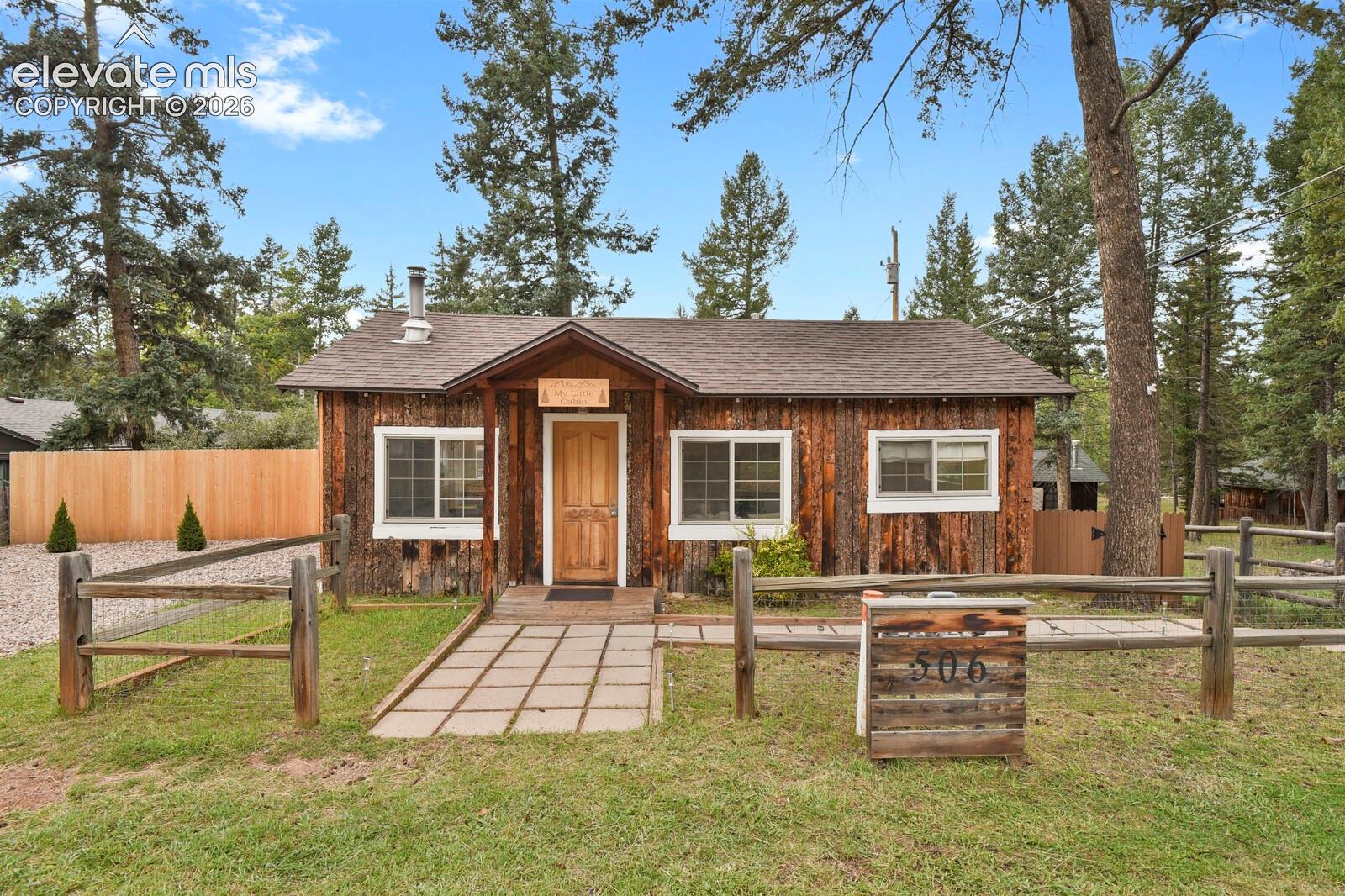 Rustic wood cabin with a fenced yard and a paved walkway leading to the front door.