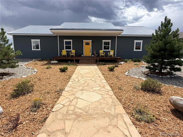 Single-story dark blue-gray home with a metal roof, yellow front door, and stone walkway.