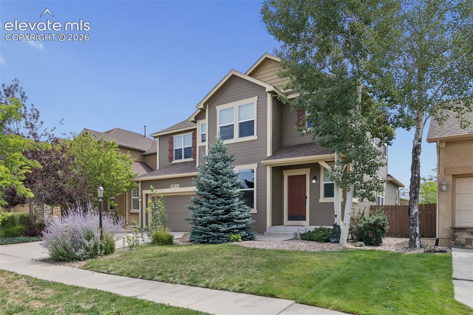 Two-story taupe house with cream trim, red front door, attached garage, and landscaped front yard.