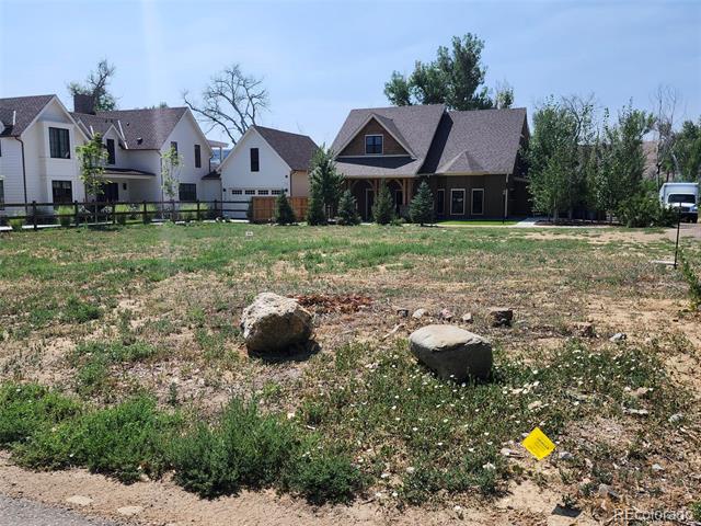 Vacant residential lot with scattered rocks and neighboring houses across the back.