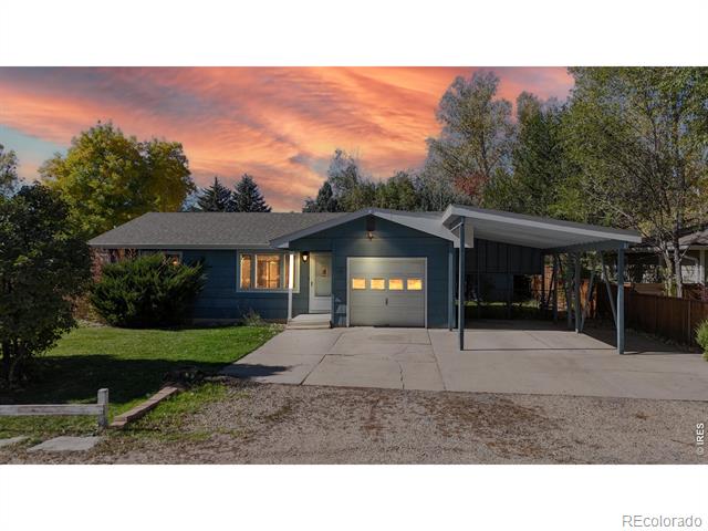 Blue single-story house with an attached garage and covered carport beneath a pink sunset sky.