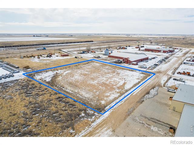 Snow-dusted vacant land parcel outlined in blue, surrounded by industrial buildings and dirt roads.