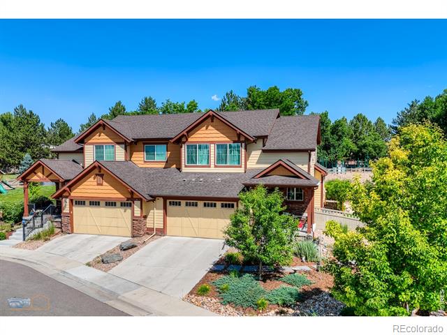 Two-story tan house with multiple gabled roofs, two garage doors, and a landscaped front yard.