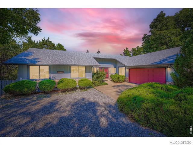 Ranch-style home with a red garage door, landscaped shrubs, and a gravel driveway at dusk.
