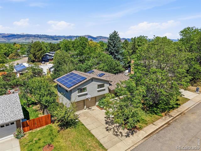 Aerial view of a two-story home with rooftop solar panels amid mature trees.